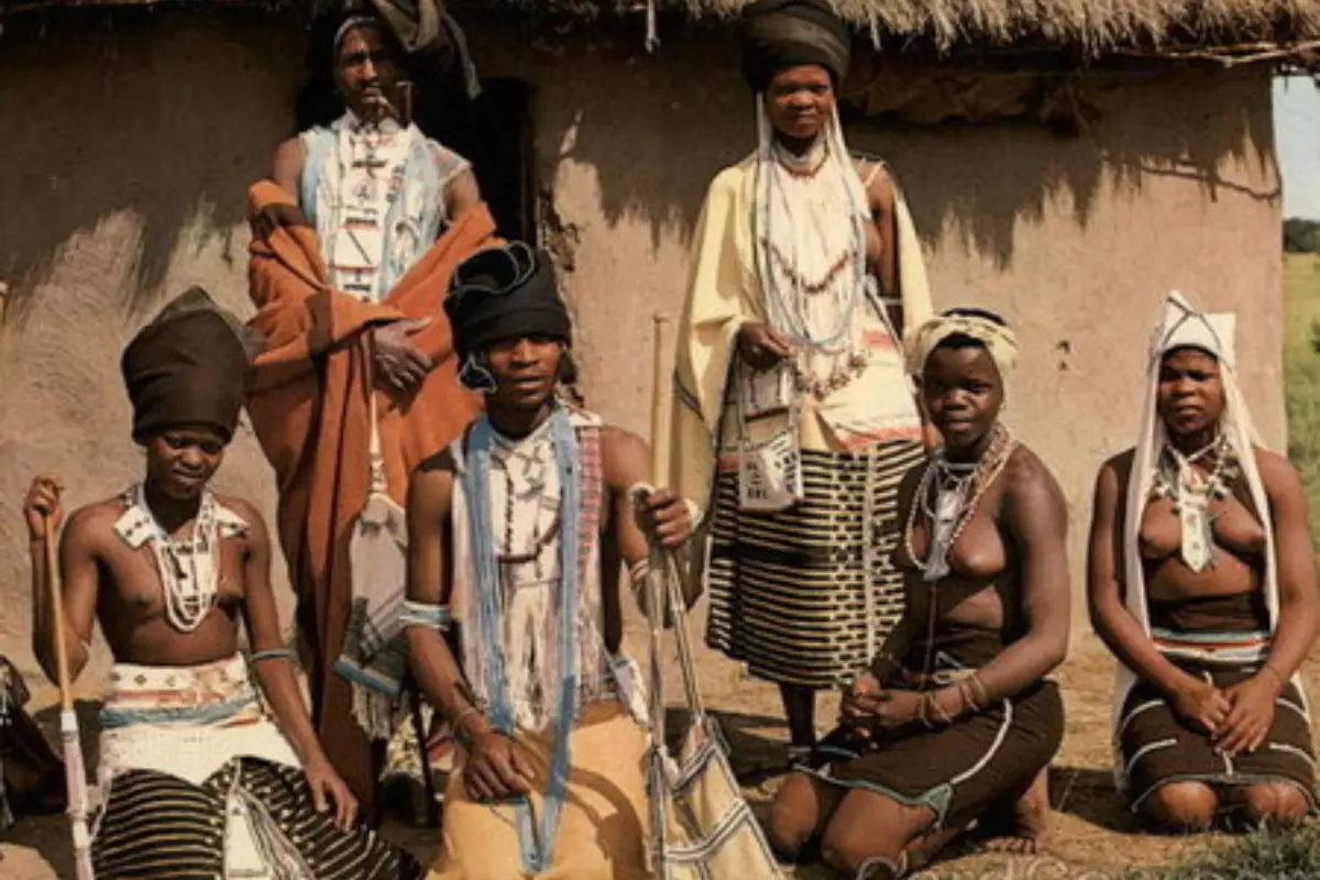 Amapondo people in traditional beaded clothing and headdresses gathered outside a mud hut in Pondoland, Eastern Cape