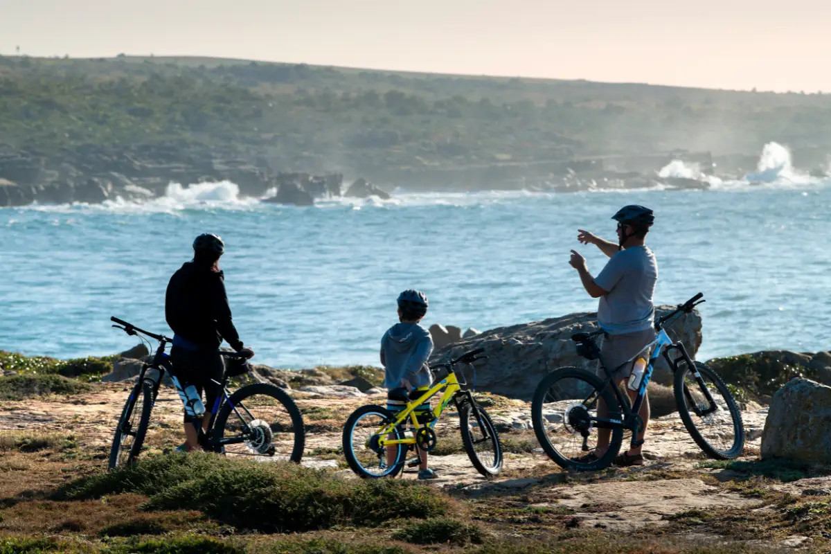 Family with mountain bikes silhouetted against crashing waves on the rocky Wild Coast shore at Mkambathi Nature Reserve