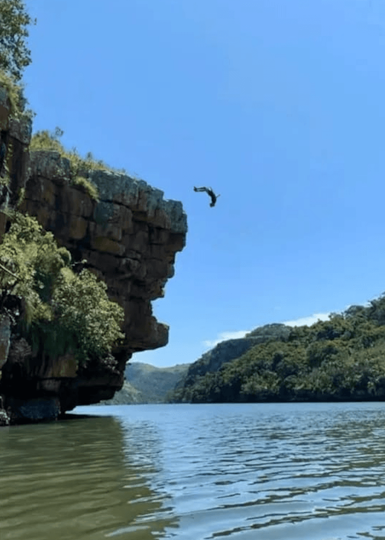 Hiker jumping off Suicide Rock overhang into the Mtentu River gorge on South Africa's Wild Coast