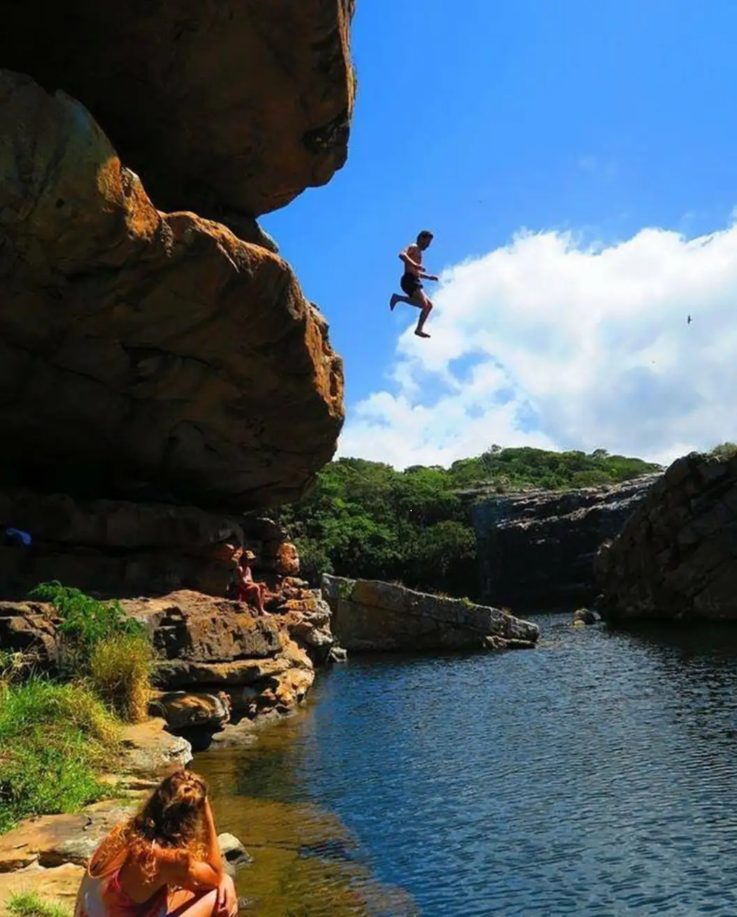 Hiker leaping off Baboon Cave rock into the turquoise Jacuzzi Hole natural pool at Mkambathi, Wild Coast