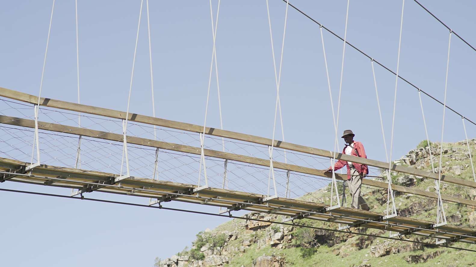 Hiker in red jacket walking across the Mzamba pedestrian suspension bridge, Wild Coast South Africa