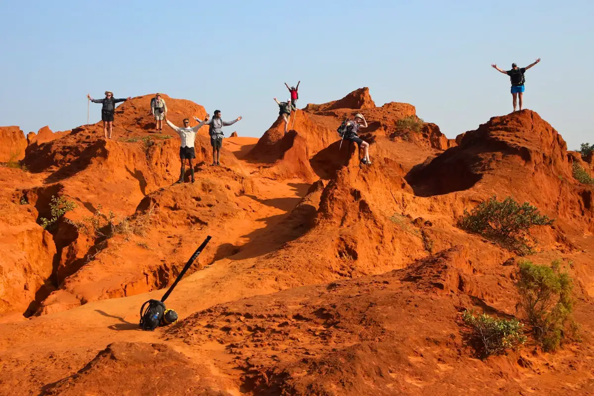Hikers celebrating with arms raised on Mtentu's vivid iron-red sand dunes at golden hour, Wild Coast South Africa