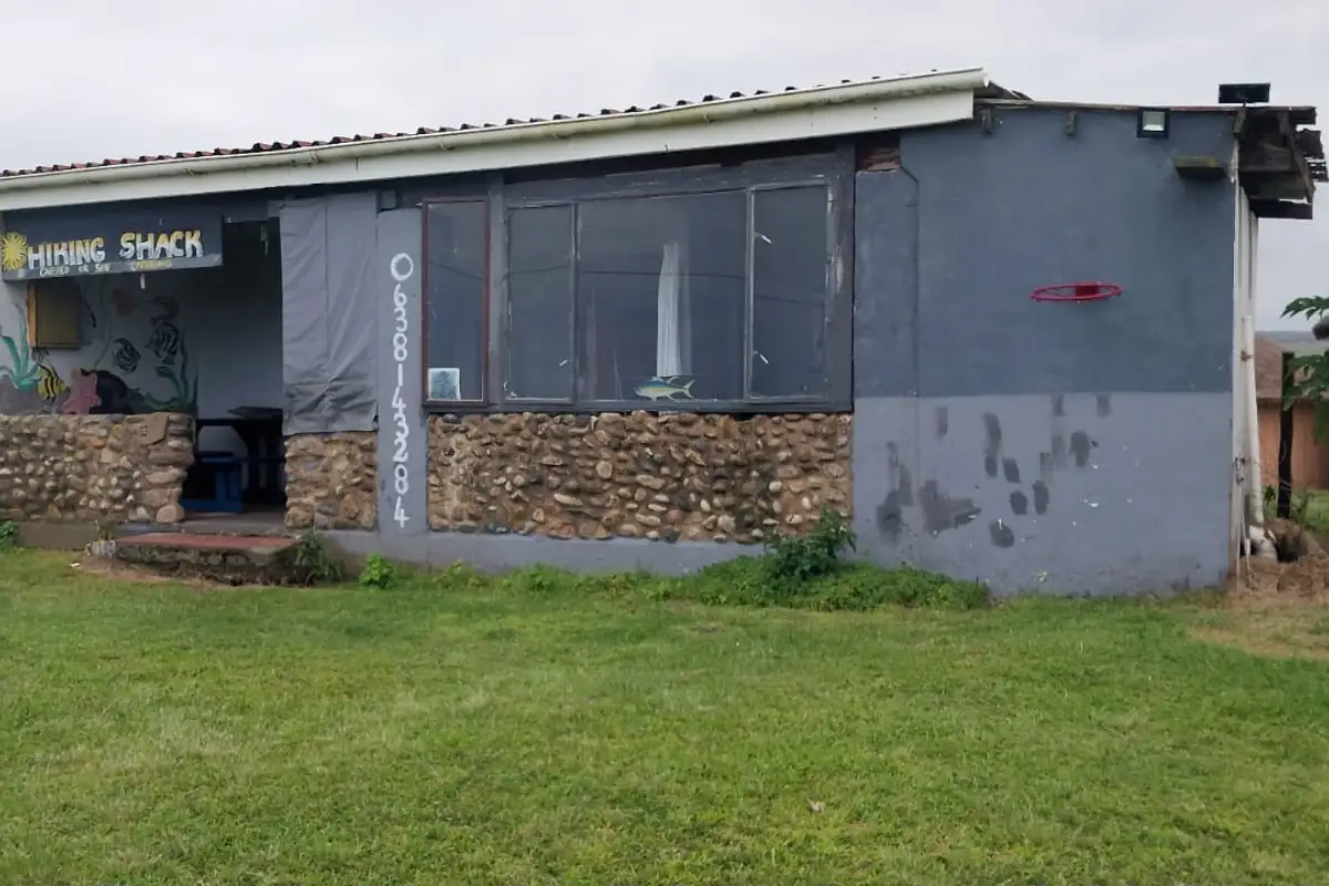 Exterior of the Hiking Shack stopover on South Africa's Wild Coast, grey building with stone wall and green lawn