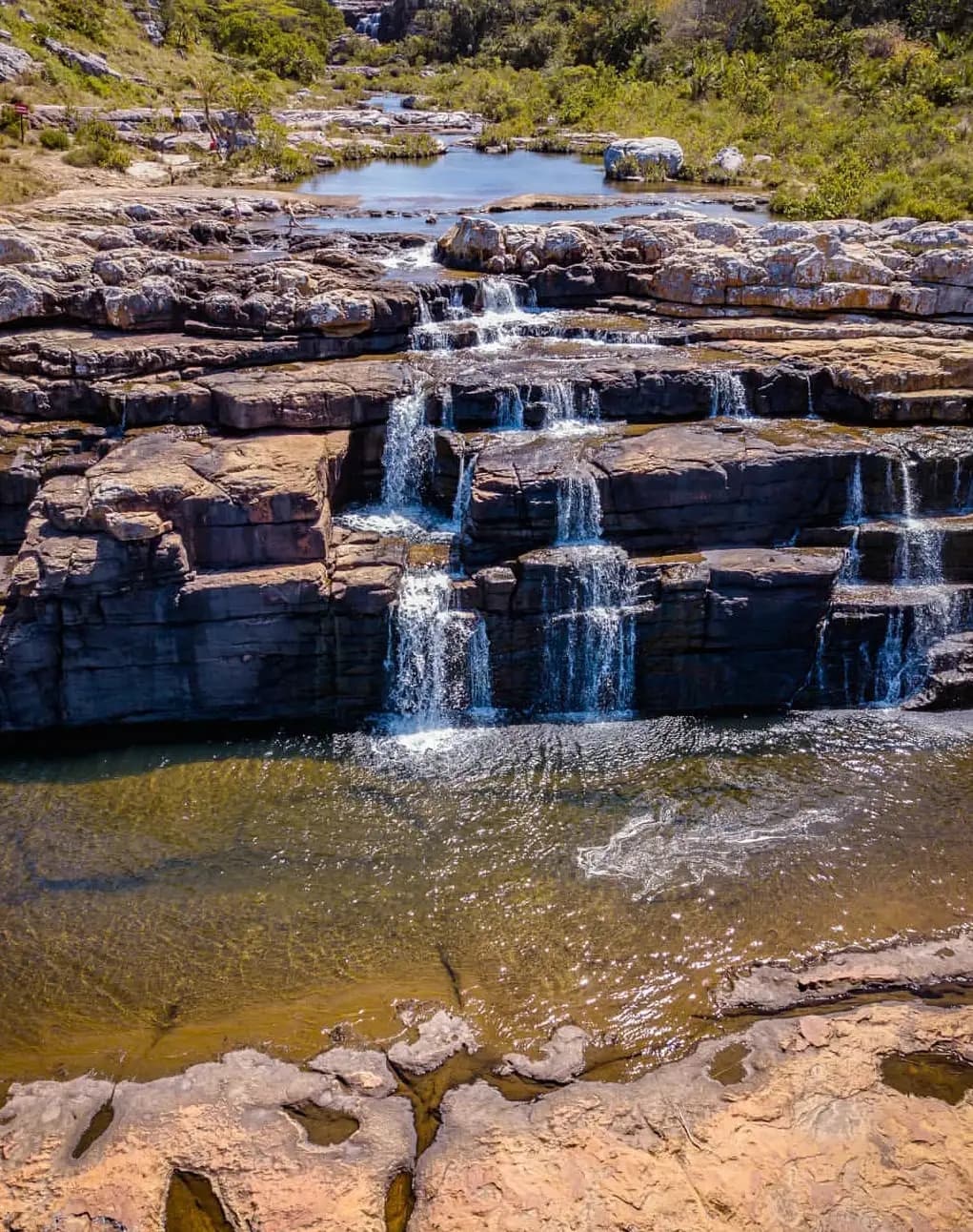 Mkambati Falls tumbling in tiered cascades over layered rock ledges into a clear pool, Wild Coast South Africa