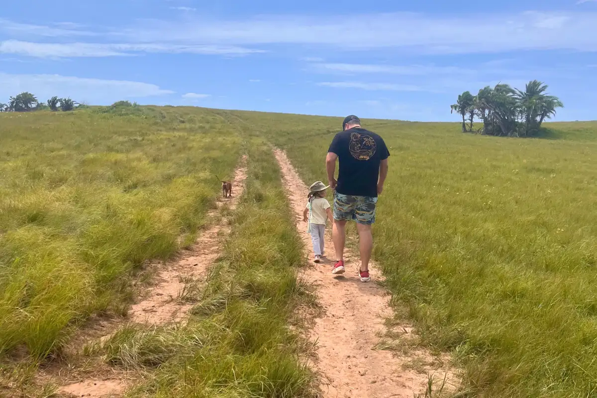 Adult and child walking hand in hand along a sandy trail through open green Wild Coast grassland, Pondoland