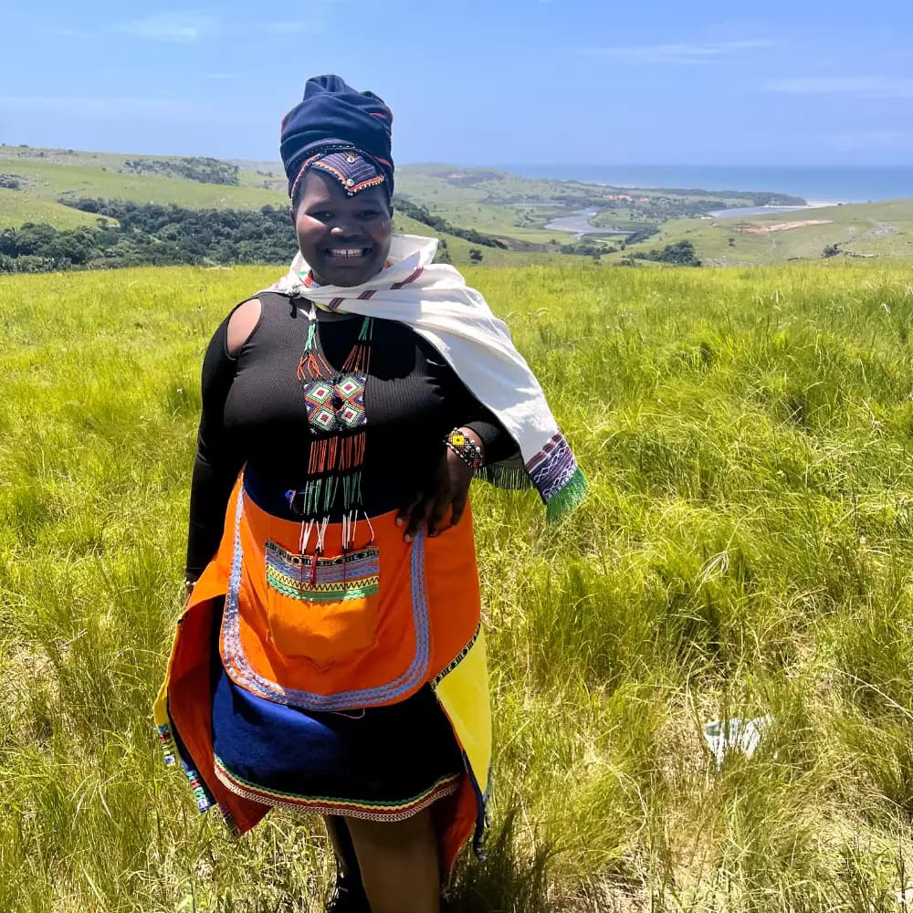 Mpondo woman in vibrant traditional beaded dress standing in coastal grasslands above the Wild Coast, Eastern Cape