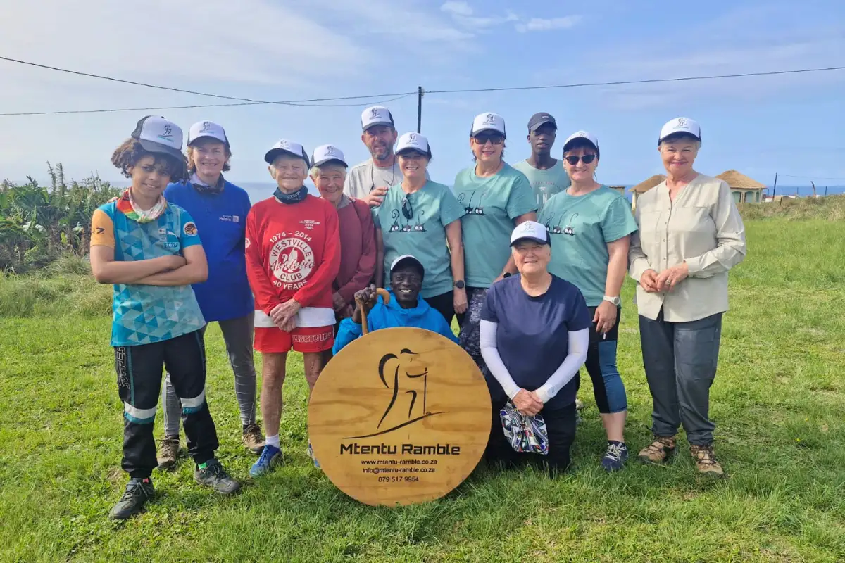 Hiking group posing around the Mtentu Ramble wooden sign on green coastal grassland, Wild Coast South Africa