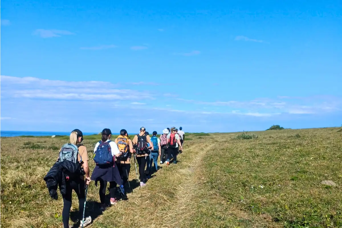 Line of hikers walking single file along an open grassy coastal trail toward the ocean, Wild Coast South Africa