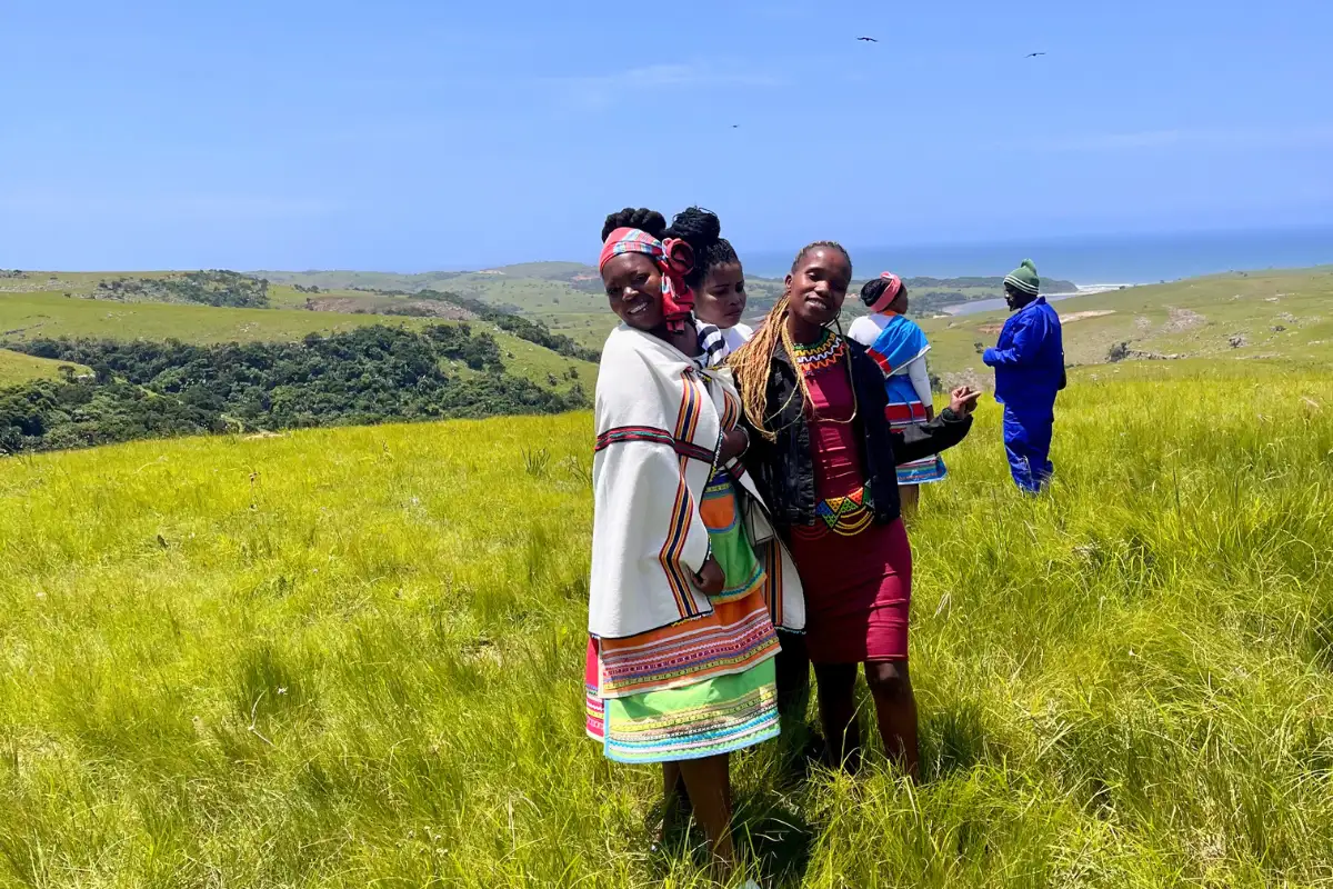 Three Pondo women in traditional colourful dress standing in green coastal grassland above the Wild Coast, Eastern Cape