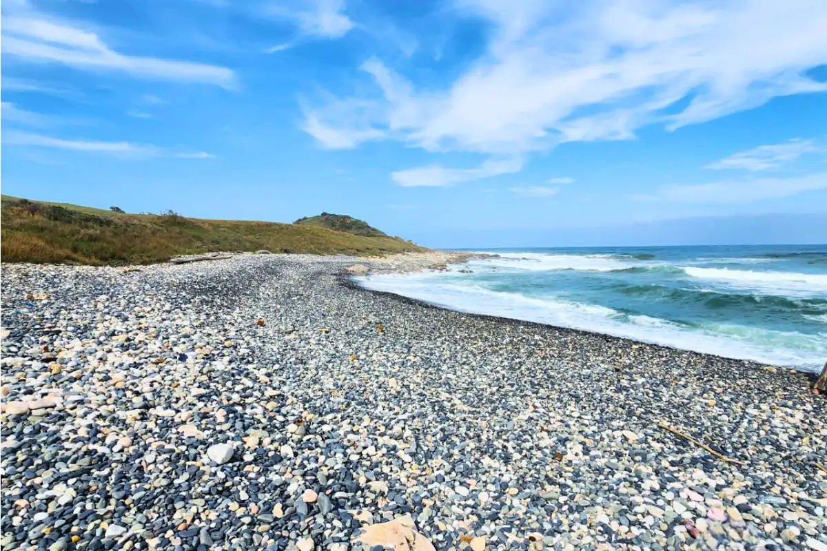 Rocky pebble beach at Skate Bay near the Hiking Shack with surf breaking under blue Wild Coast sky