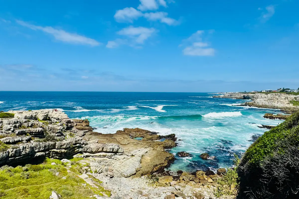 Wild Coast rocky shoreline with white surf crashing over boulders under a blue sky, the unforgiving coastline that has swallowed hundreds of ships