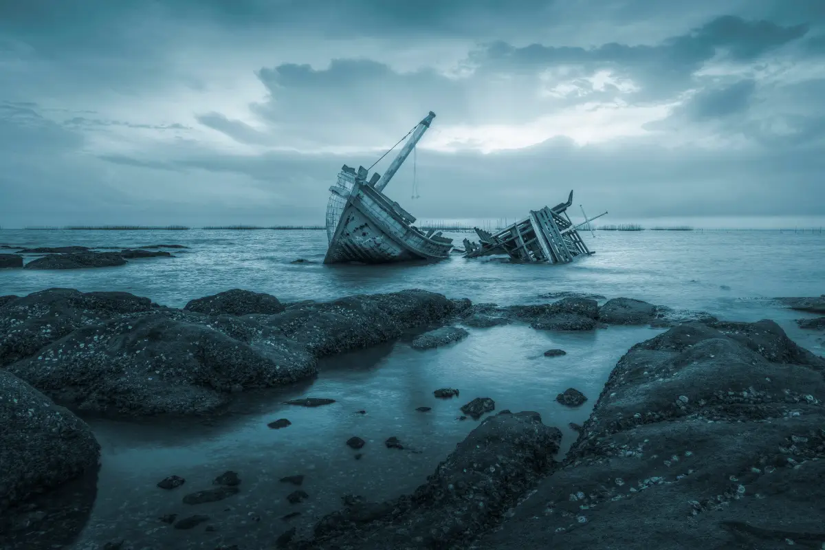 Broken fishing vessel listing on rocky Wild Coast shoreline at dusk, a haunting wreck silhouetted against stormy blue coastal skies
