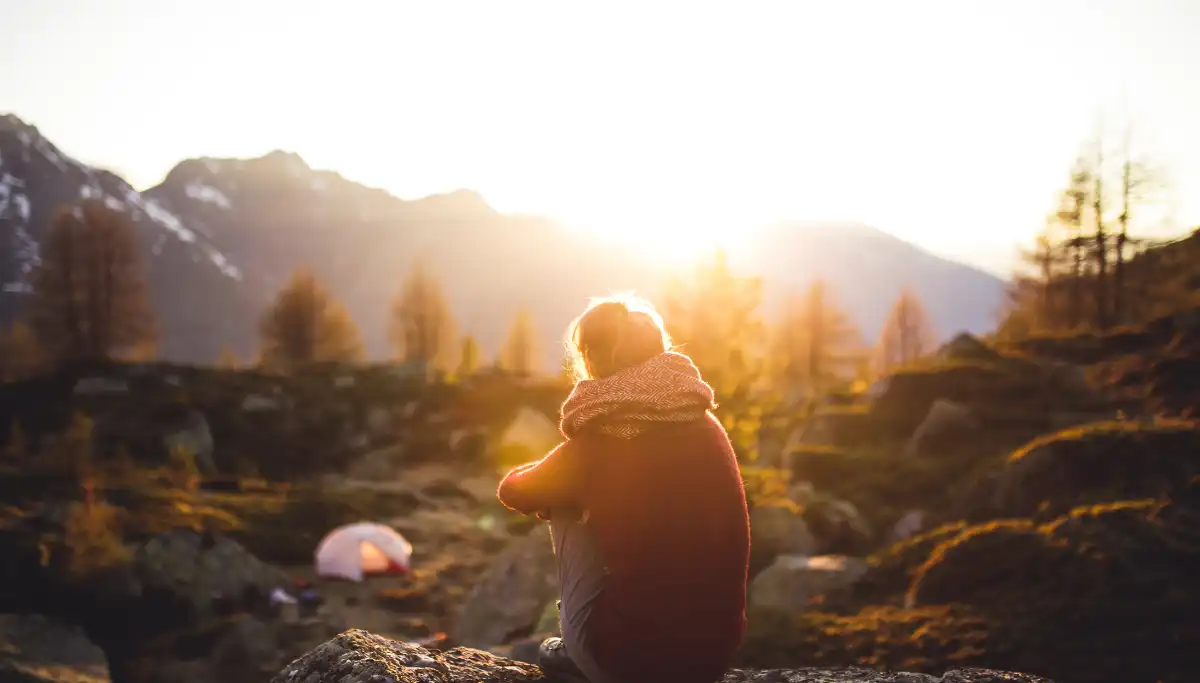Solo hiker sitting on a rock watching a blazing golden sunset over a mountain valley in South Africa, tent visible in the background