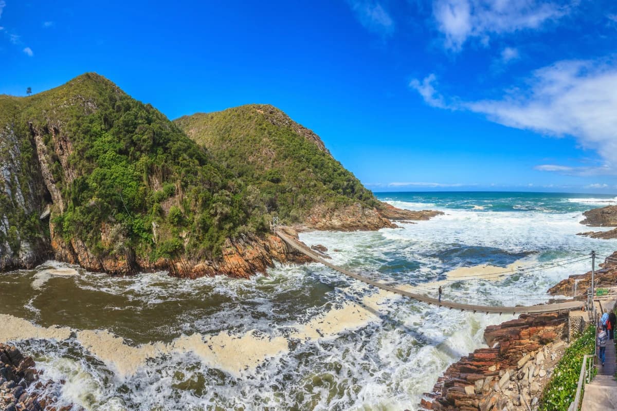 The suspension bridge across the mouth of the Storms River on the Otter Trail, waves surging into the gorge beneath forested cliffs, Tsitsikamma, Garden Route, South Africa